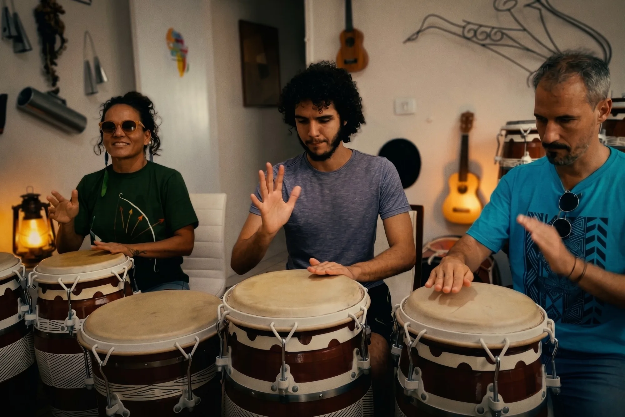 Três alunos da Casa Cangoma em aula prática de percussão, tocando tambores conga em um estúdio acolhedor e profissional em São José dos Campos.
